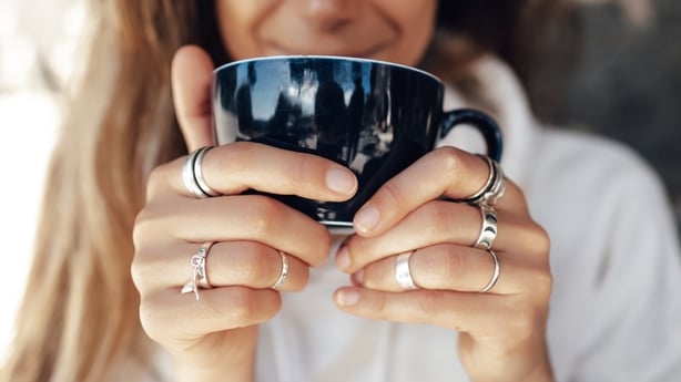 Nærbillede hånd af kvinde, der holder en kaffekop og bærer sølvringe