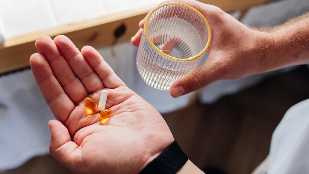 Nærbillede af person, der forbereder sig på at tage vitamintilskud med et glas vand derhjemme. Daglig wellness, sundhedsrutine og selvplejekoncept.