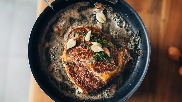 Overheadbillede af kok, der forbereder ribeye med smør, timian og hvidløg. Keto diæt.