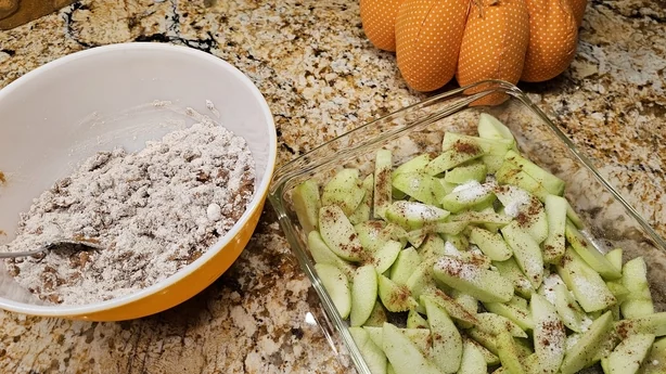 Skiver af Granny Smith æbler sammen med mel, muskatnød og kanel i en skål, gør dig klar til at blande ingredienser til en lækker sæsonbestemt yndlingsdessert.